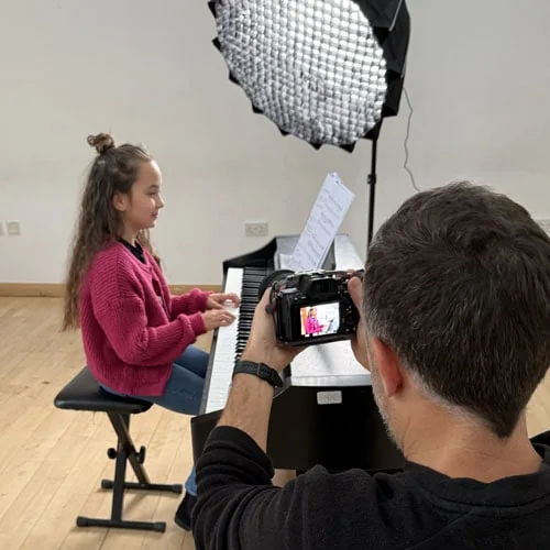 brown hair girl playing piano whilst someone is taking photos