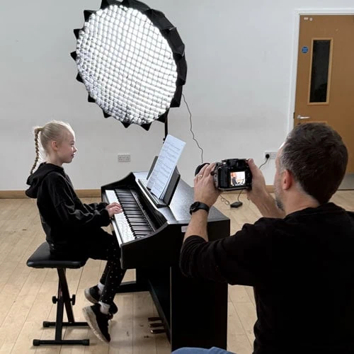 blonde girl playing piano whilst someone is taking photos