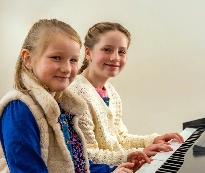 two girls smiling whilst playing piano